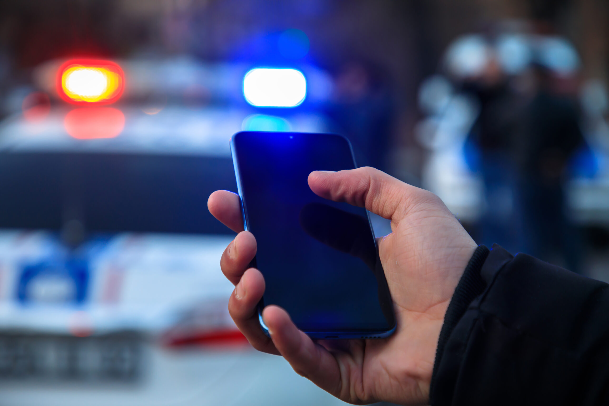 man holding phone with police in street